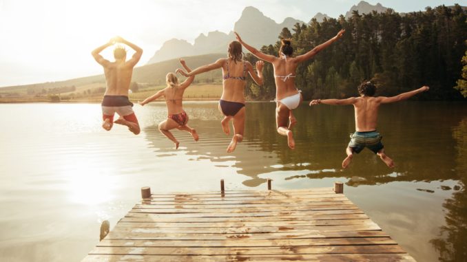Young friends jumping into lake from a jetty